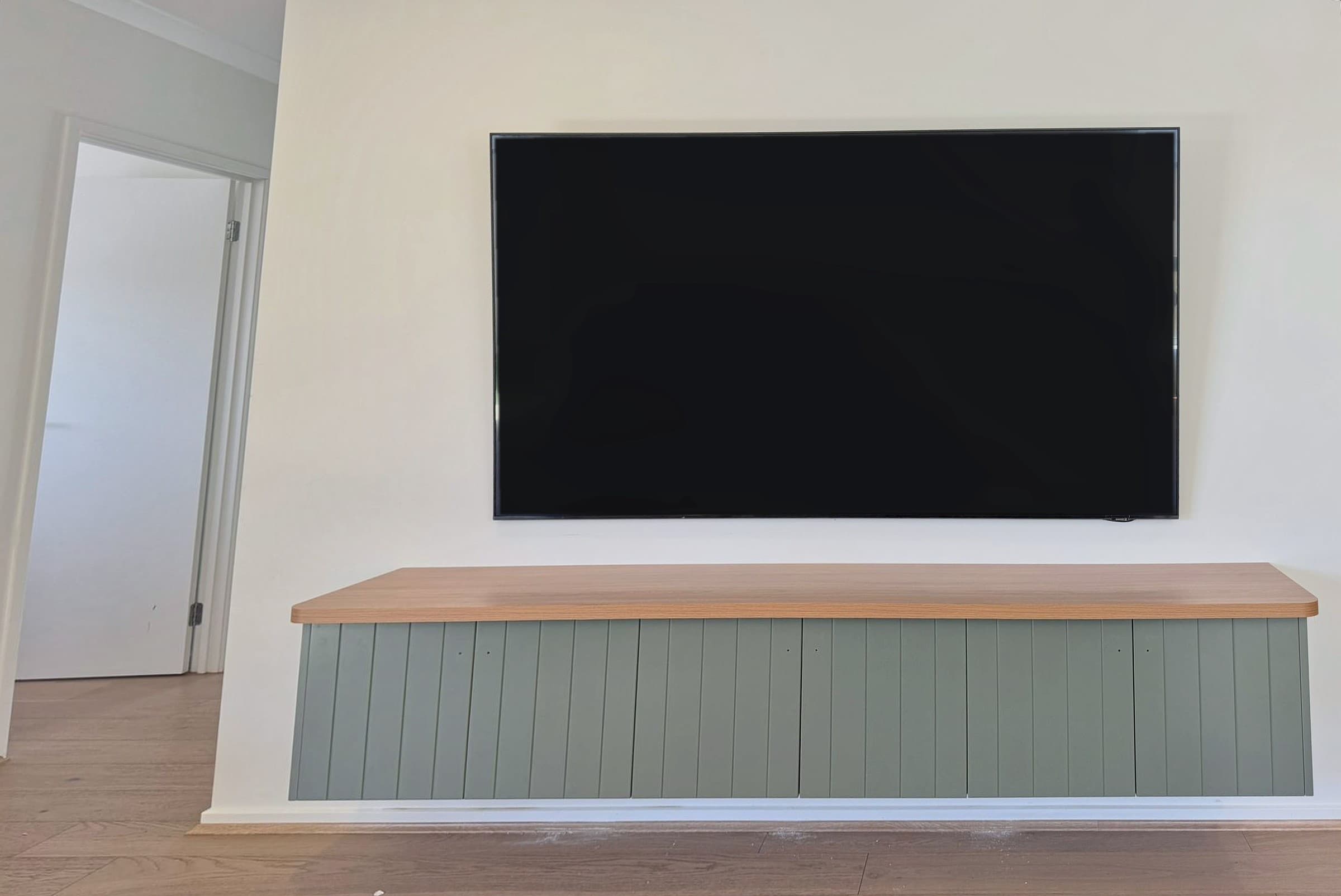Wall-hung entertainment unit: sage green V-groove doors under a warm timber-look benchtop.