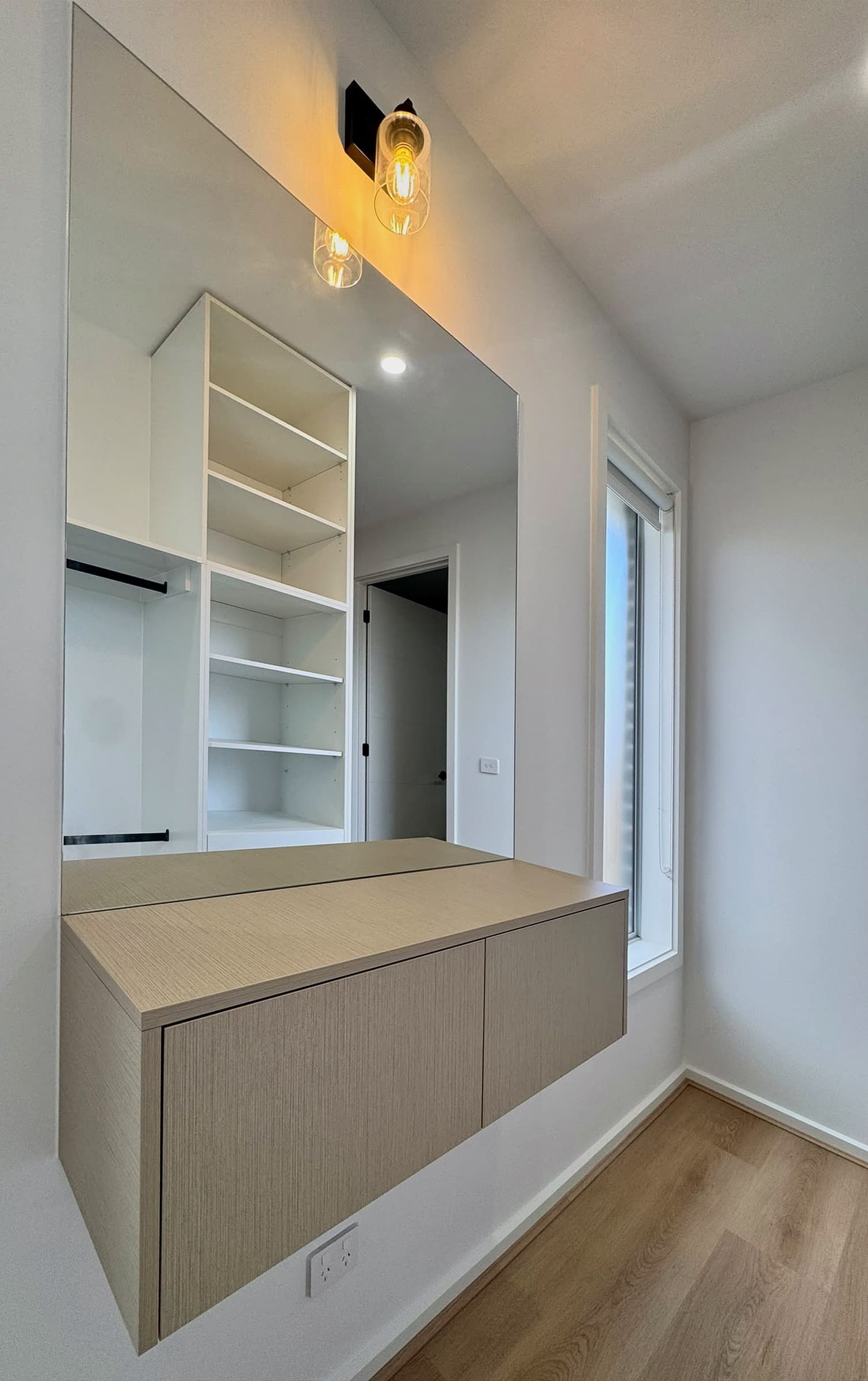 Floating dressing vanity in pale oak-look finish beneath a full-width mirror.