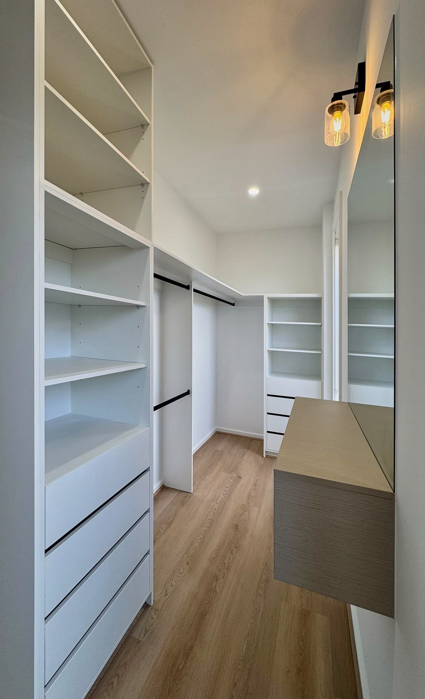 White walk-in robe with adjustable shelving, drawer stacks, double hanging and a floating oak-look vanity.