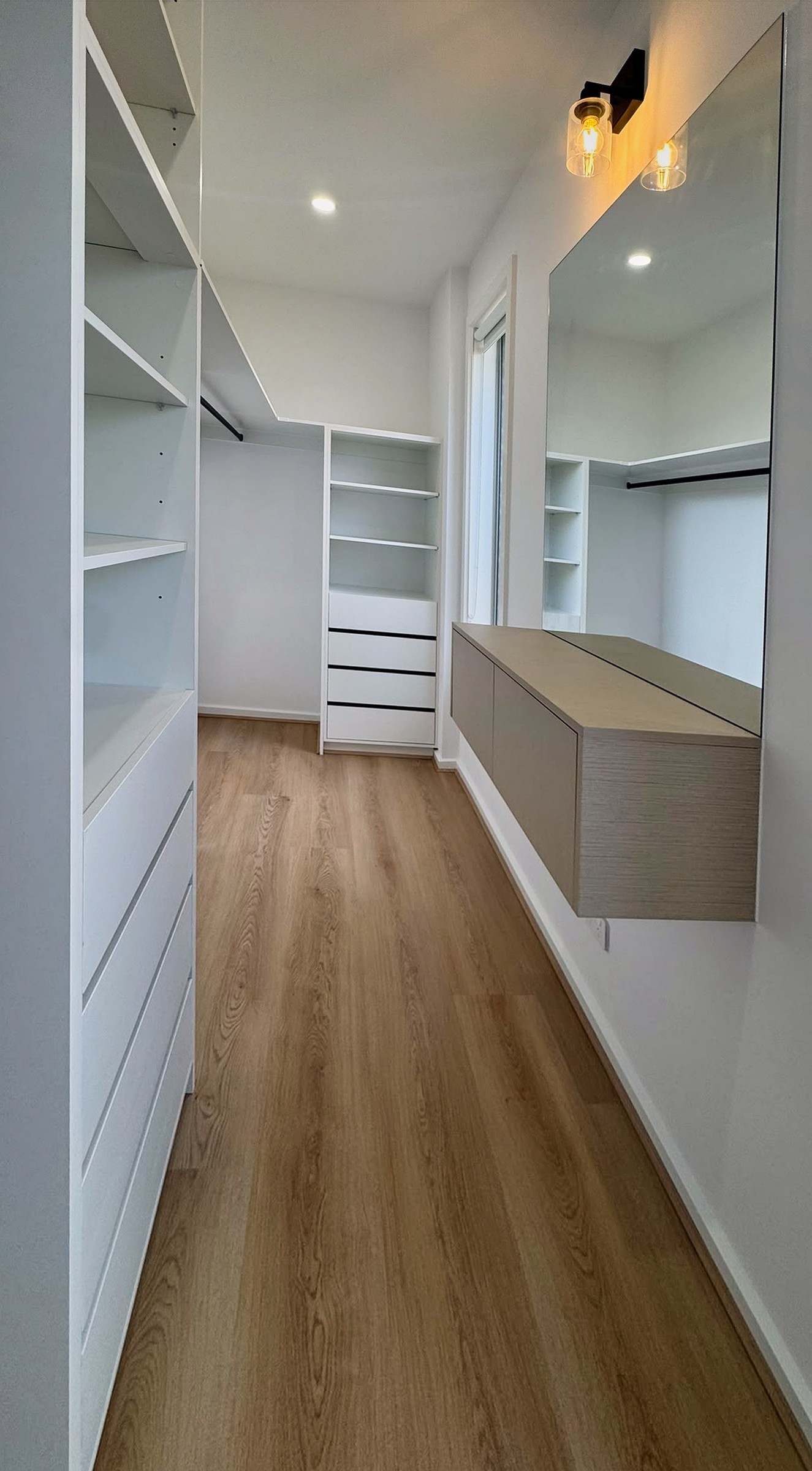Walk-in robe in crisp white with open shelving, hanging rails, drawers and a floating oak-look dressing bench.